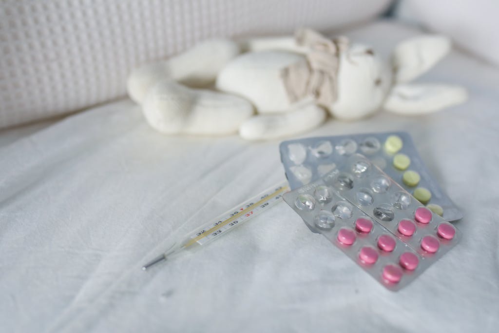 Close-up of medication and thermometer on a bed beside a plush rabbit toy, symbolizing childhood illness care.