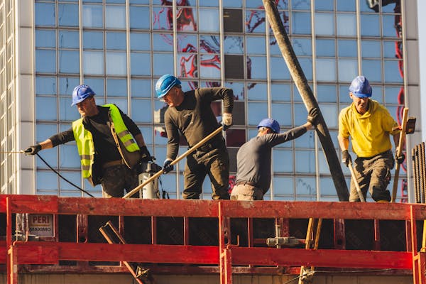 A group of construction workers in safety gear actively working on a high-rise building site.